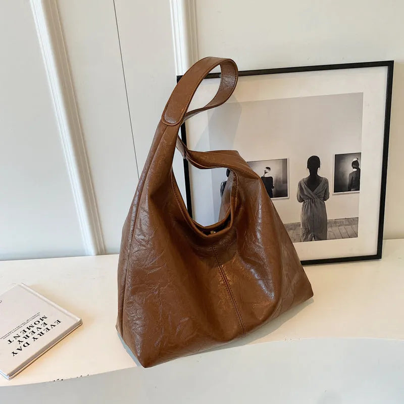 Soft black PU leather shoulder bag with large compartment and adjustable strap on a plain background.
