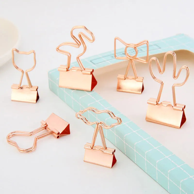 Small gold-plated metal office clip with a long tail, shown in a choice of flamingo, love, clouds, cat, and cactus shapes.