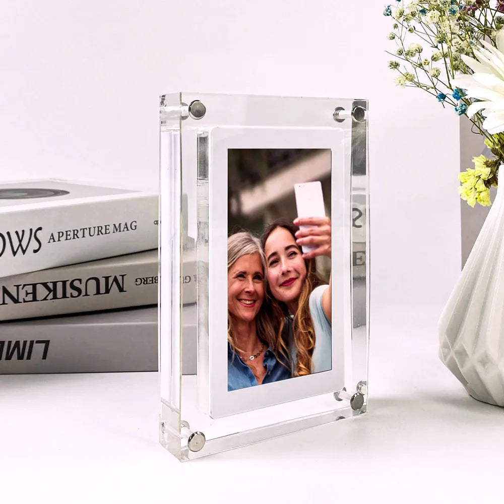 White vertical digital picture frame with acrylic casing on a table, showing a family photo on screen.