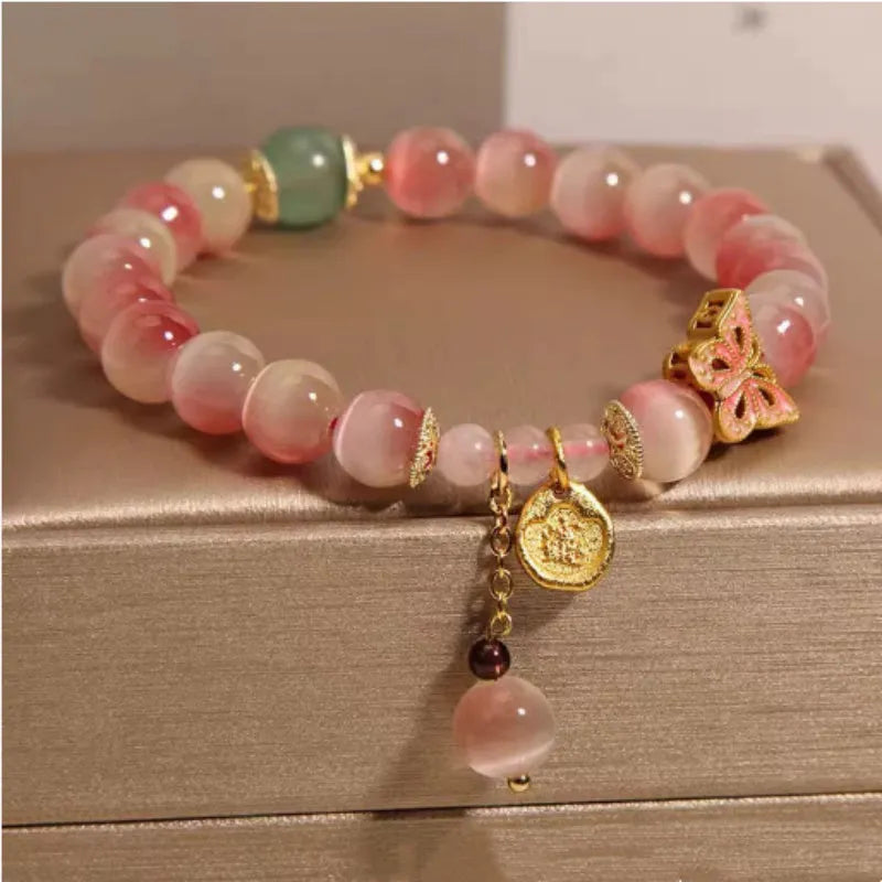 Close-up of a women's bracelet with a pink opal butterfly charm on an electroplated chain.