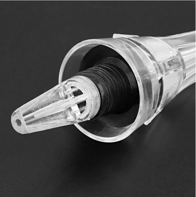 A clear acrylic wine aerator with a stainless steel filter, shown next to a wine glass.