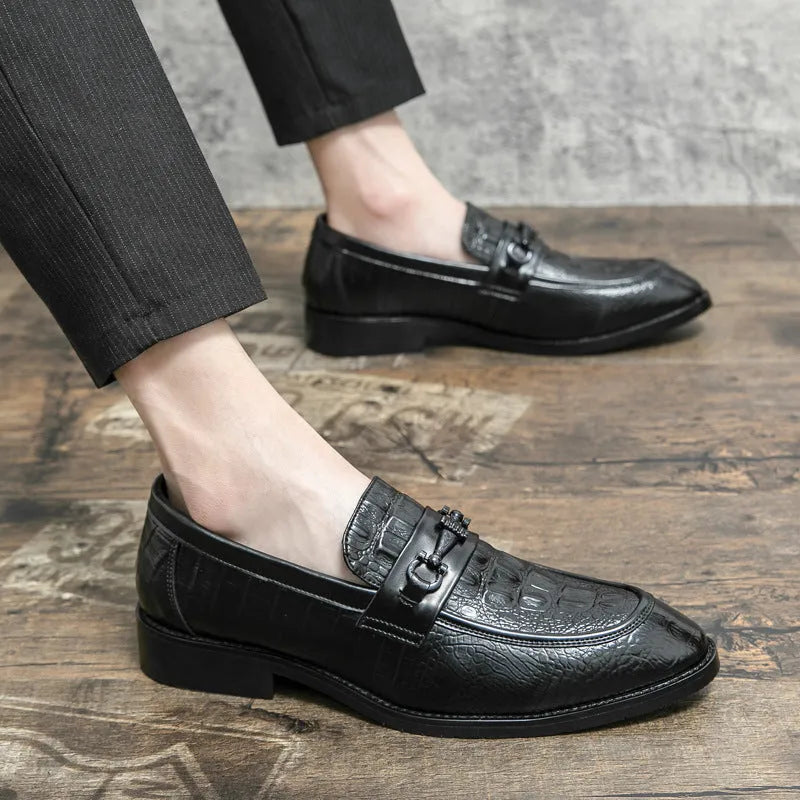 Men's black slip-on formal shoes with pointed toe and belt buckle detail on a light background