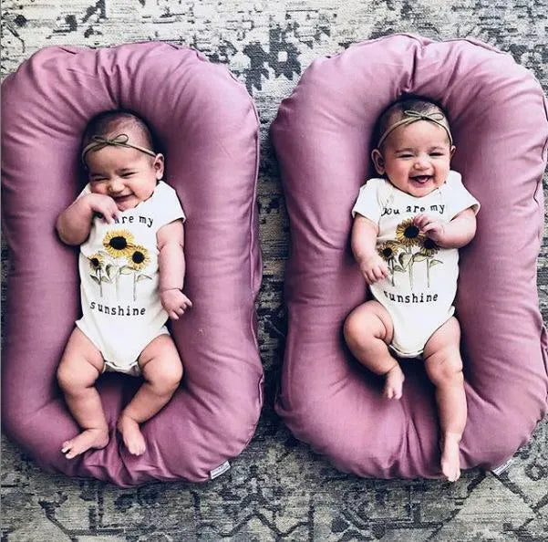 Cotton portable baby nest crib for newborns, beige colour, shown on a bed.