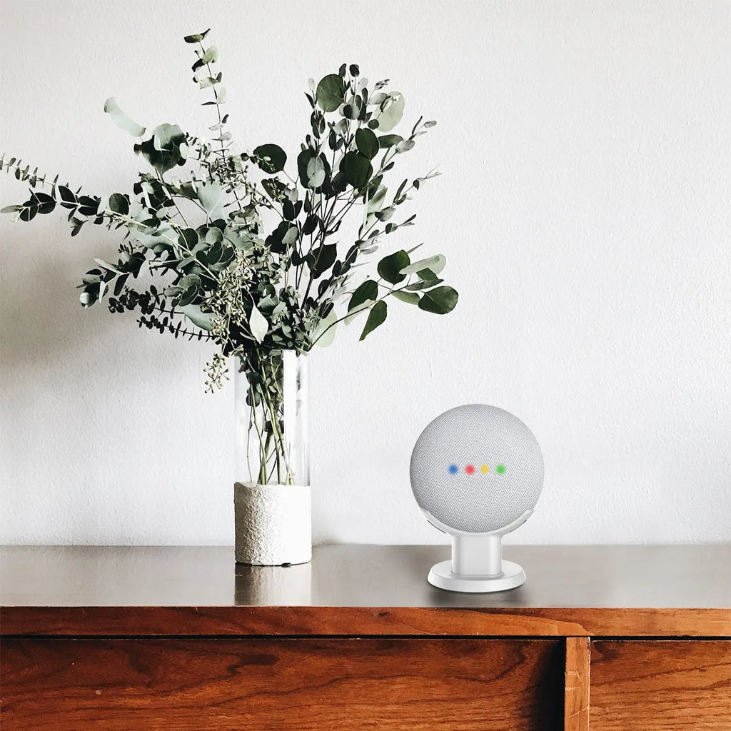 Black PlusAcc plastic stand holding a white Google Home Mini smart speaker on a wooden tabletop.