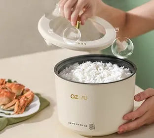 Compact round miniature rice cooker with steaming tray in blue, shown with non-stick liner and mechanical control panel.