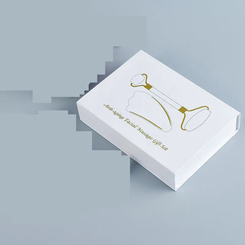 White jade facial roller and gua sha tool set with rose quartz board on a neutral background.