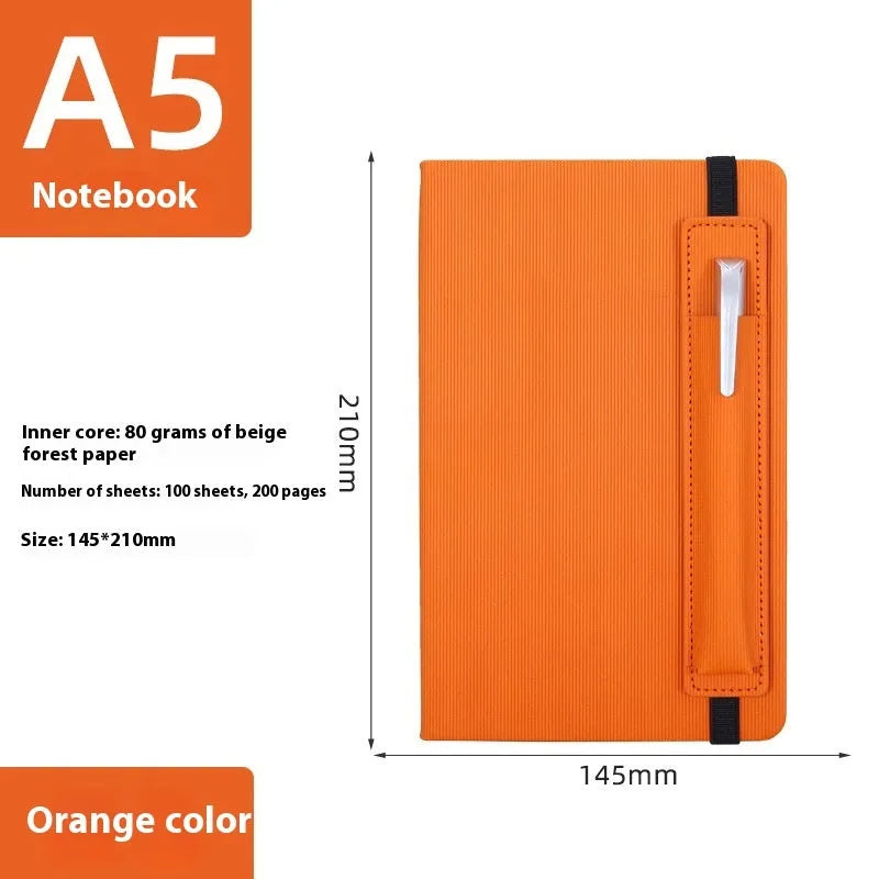 A5 faux leather notebook with pen insert and strap, open on a desk showing lined pages