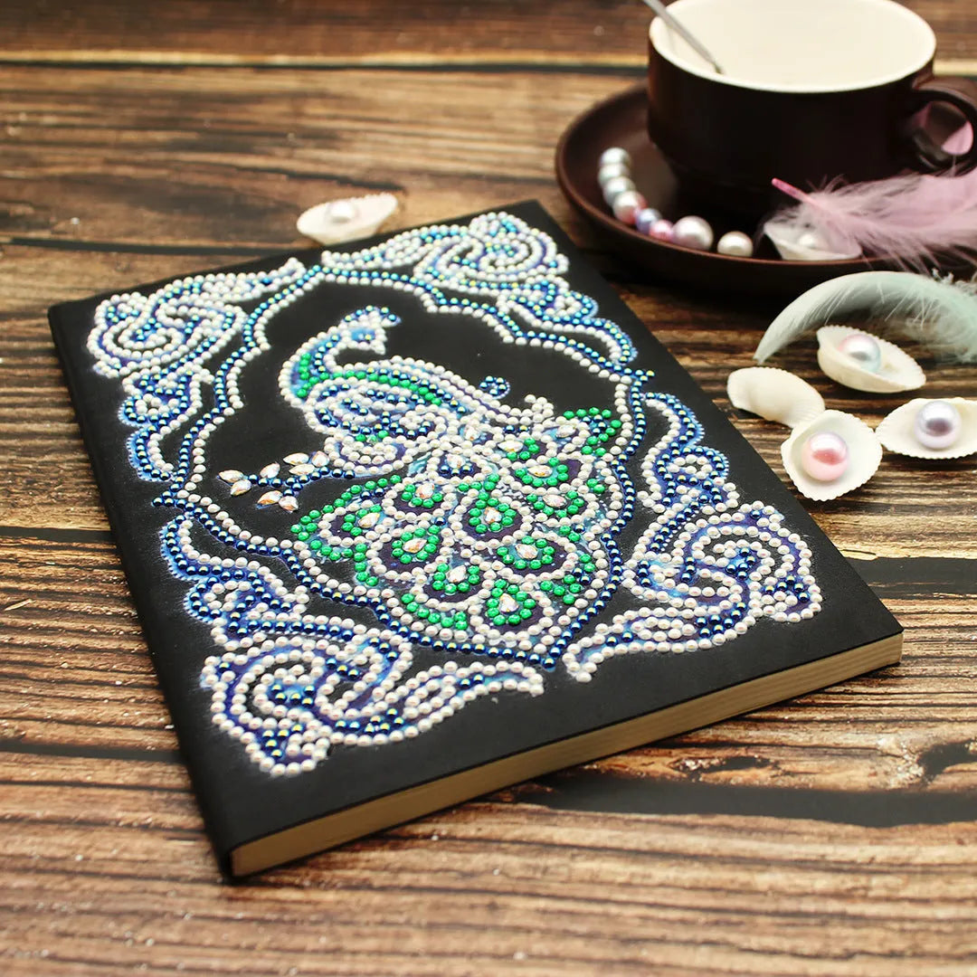 A5 black notebook with a peacock diamond painting design and packets of shaped and bright drill rhinestones.