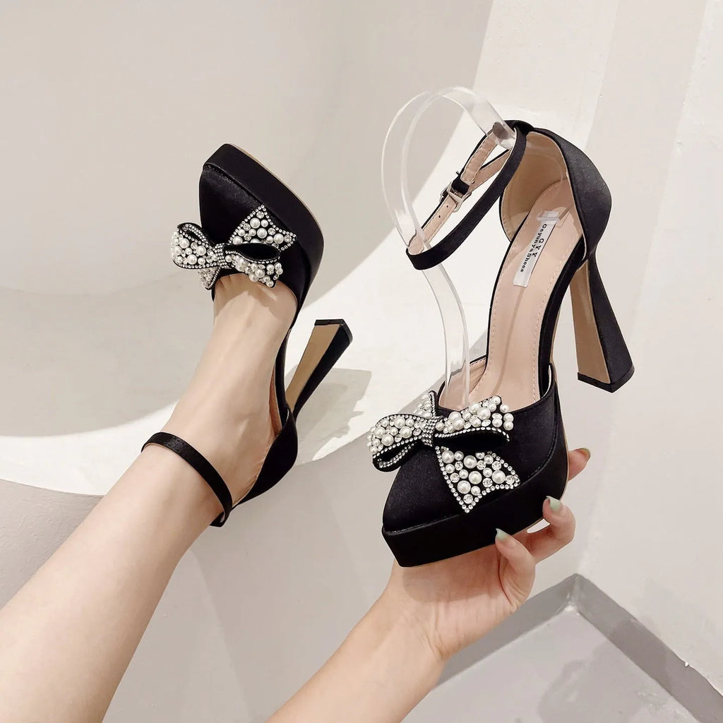 Women's black satin pointed-toe pumps with a bow and elastic loop fastening.