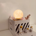 Moon planet floating LED night light with three astronaut figurines on dark surface
