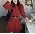 Women's long sleeve loose knitted dress in beige with a black belt, shown on a hanger.