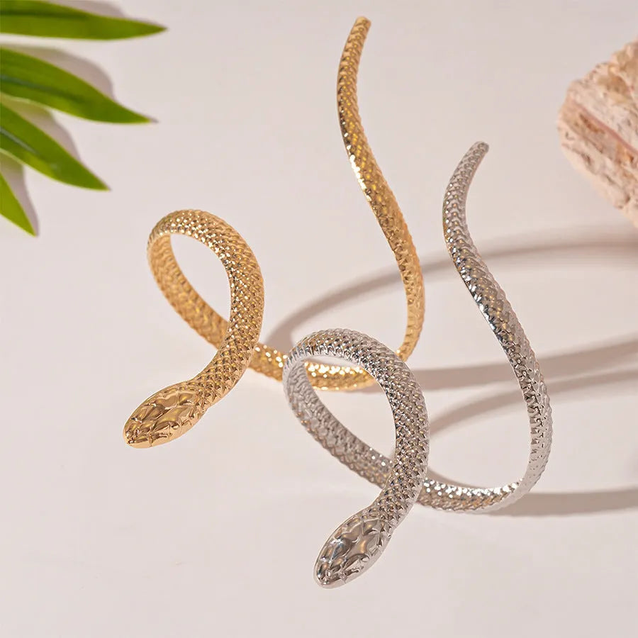 Gold exaggerated twisted snake design bracelet and ring jewellery set on a dark background.