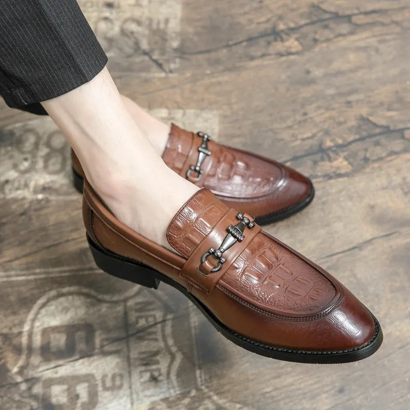 Men's black slip-on formal shoes with pointed toe and belt buckle detail on a light background