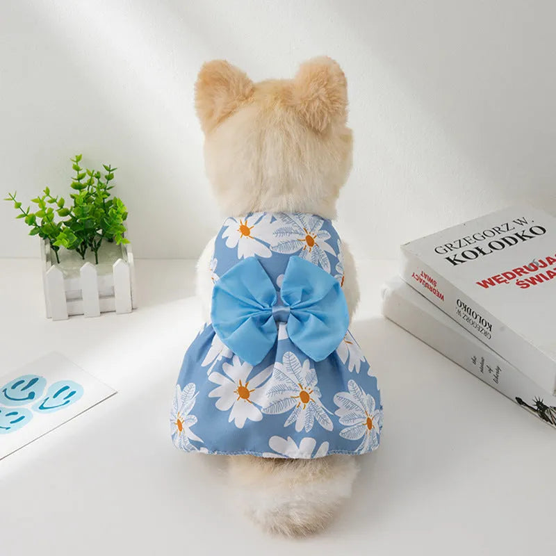 A dog or cat wearing a thin orange princess dress with a large floral butterfly knot bow.