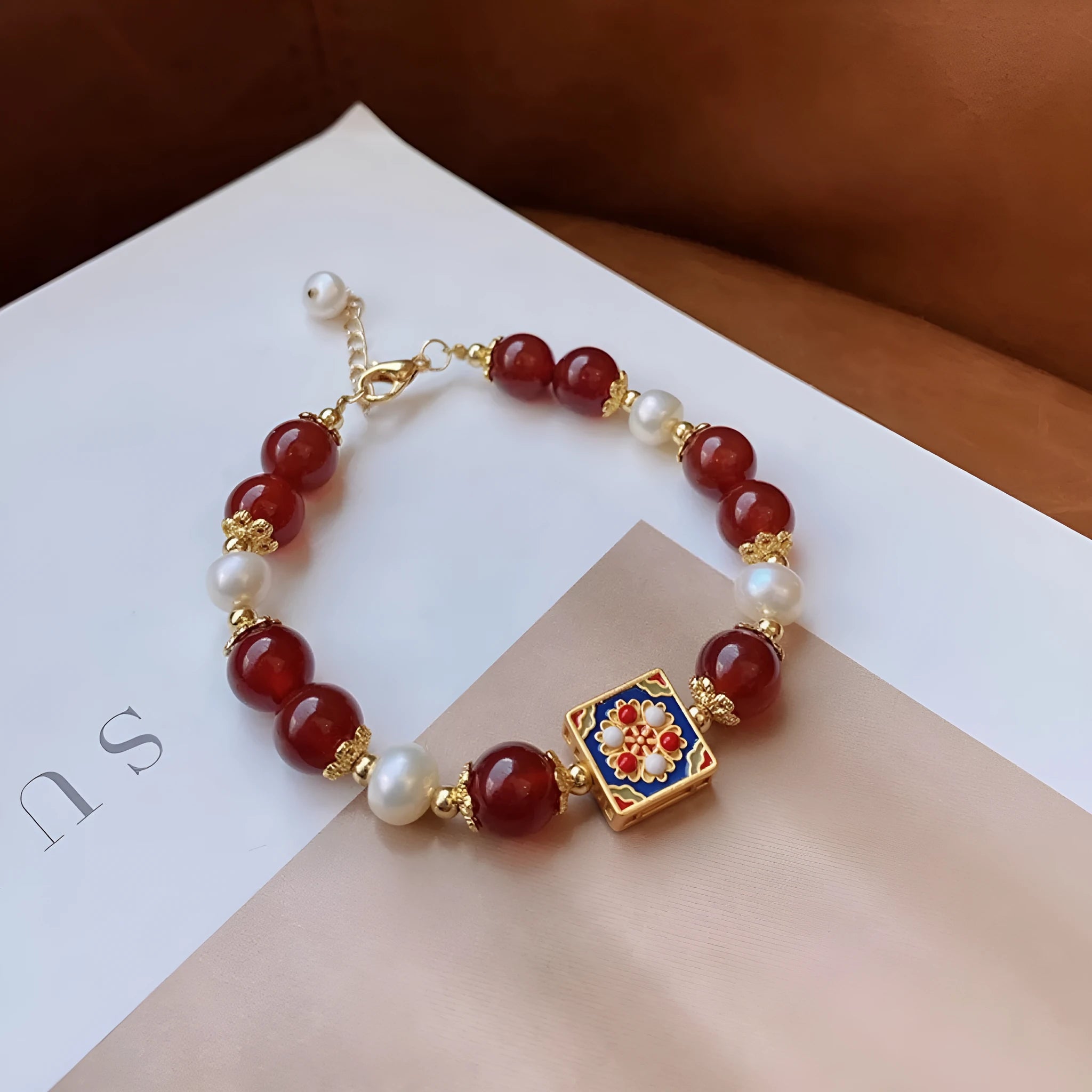 Red agate and pearl women's bracelet with constellation design on a wrist.