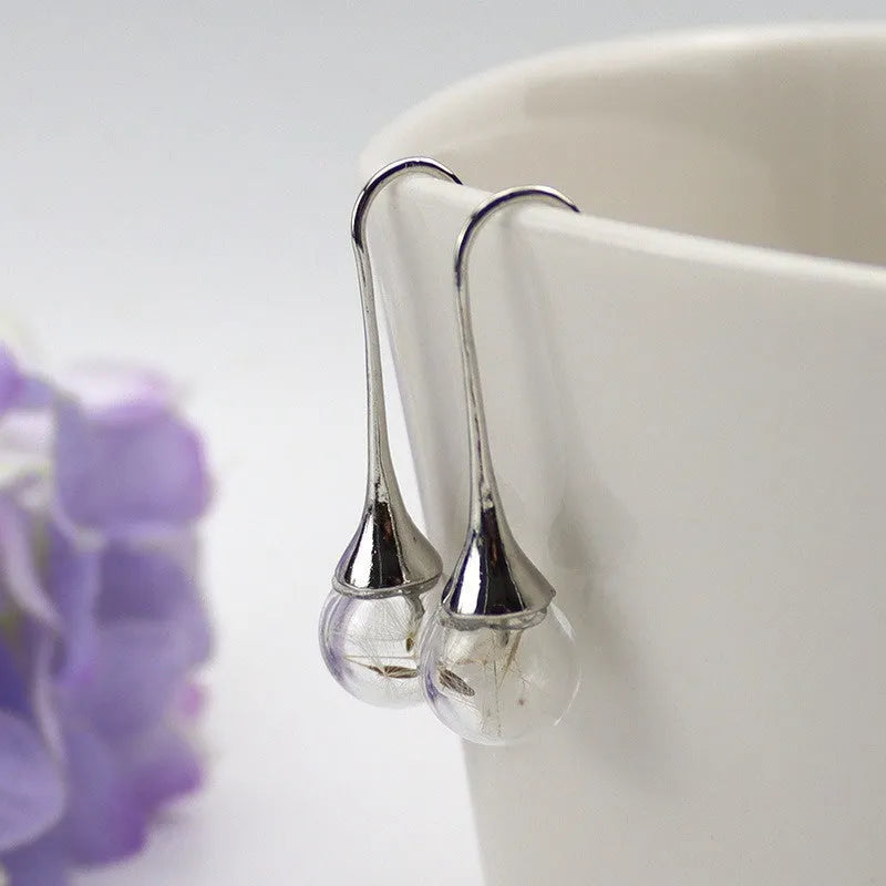Transparent glass ball earrings with a dandelion seed inside, on a silver French hook.