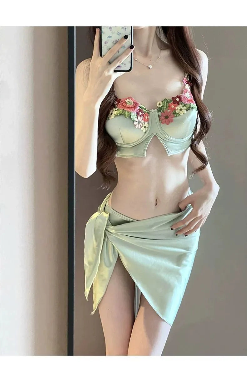 Green women's three-piece bikini set with triangle top, briefs, and skirt on hanger
