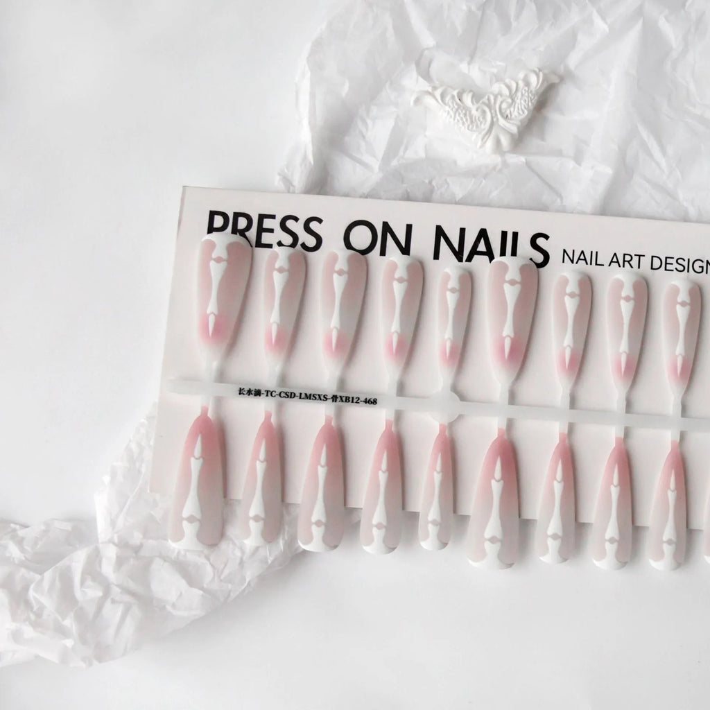 Close-up of long black and pink Christmas gothic nail tips with frosted finish on a flat surface, next to a storage strip.