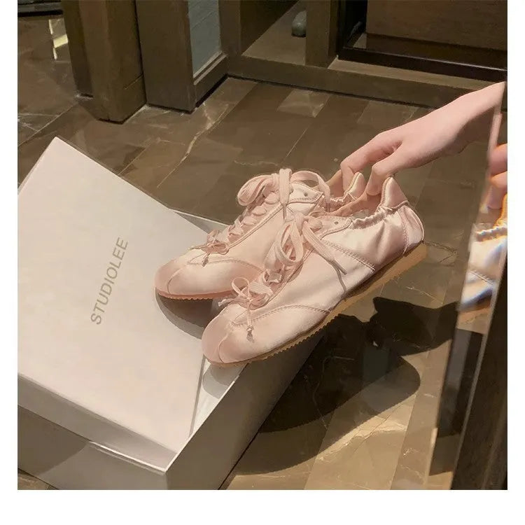 Women's champagne pink satin ballet flats with round toe and lace-up front, shown on a white background.