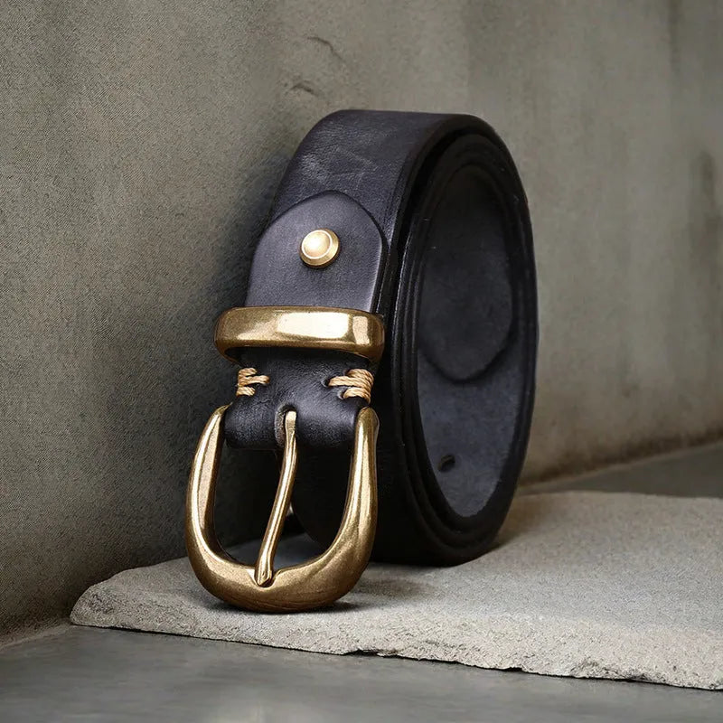 Men's black cattlehide leather jeans belt with a copper pin buckle on a wooden background.