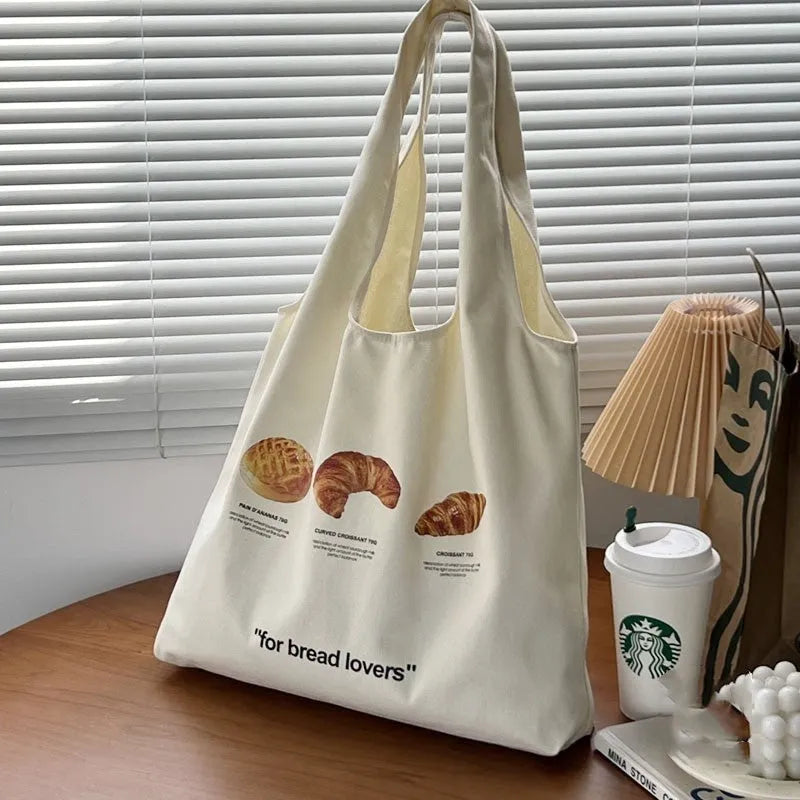 Beige canvas tote bag with bread print design showing adjustable shoulder strap and structured base