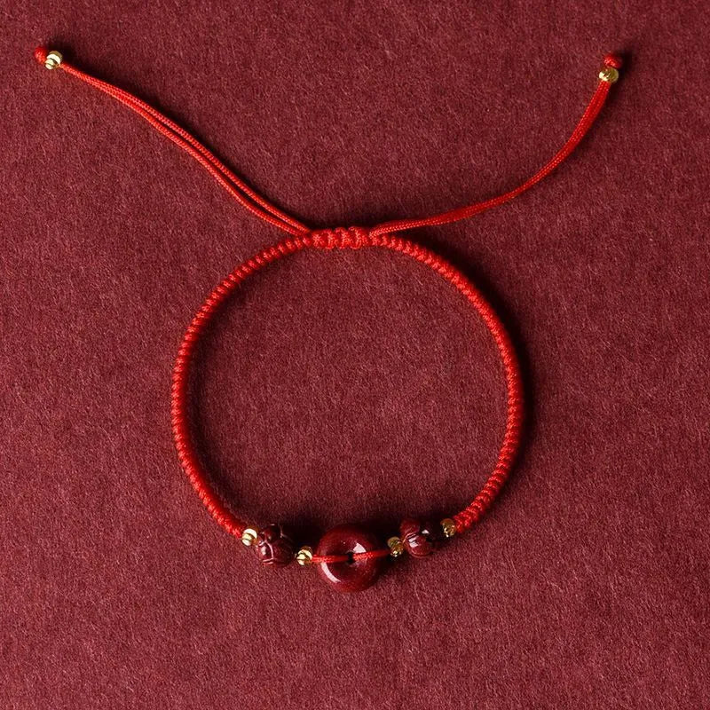 Traditional cinnabar bracelet with a heart-shaped peace buckle clasp on a red rope.