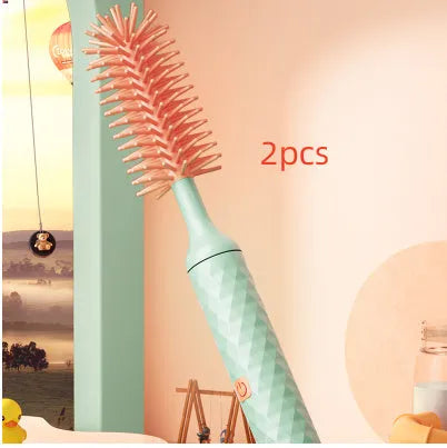 Pink and green electric baby bottle cleaning brush with rotating silicone head on a table