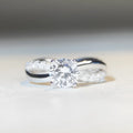 Silver geometric cross ring with a 1-karat moissanite stone on a twisted band.