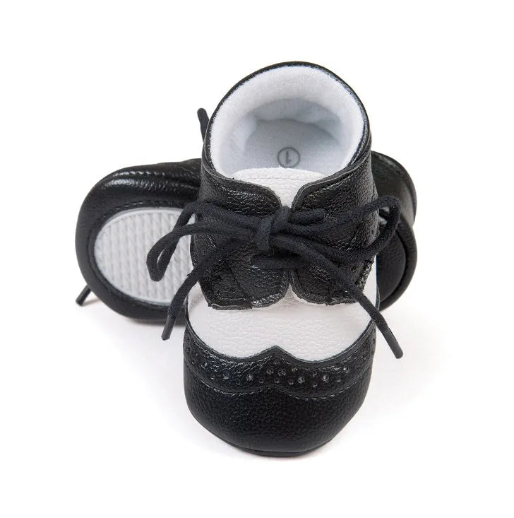 Vintage-style soft-soled baby shoes in black, grey, light brown, and white for infants 0-12 months.