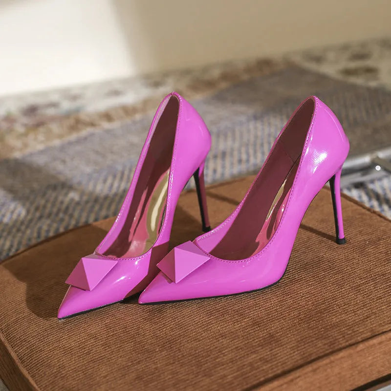 Pink patent leather women's stiletto heels with pointed toe, rivet decor, and a buckle.