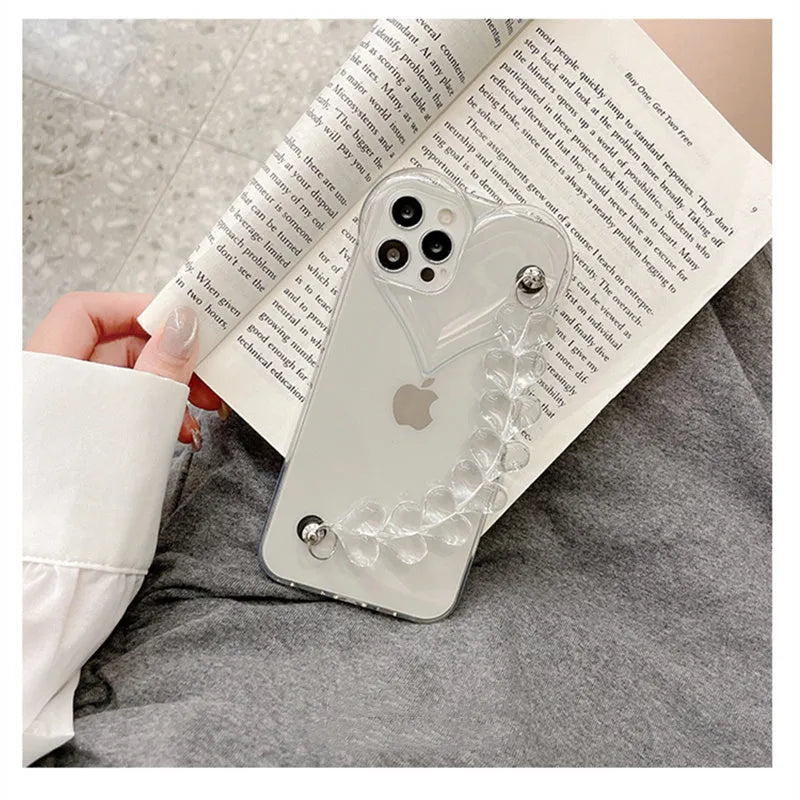 Clear iPhone case with transparent love heart bracelet charm attached, showing soft TPU material.