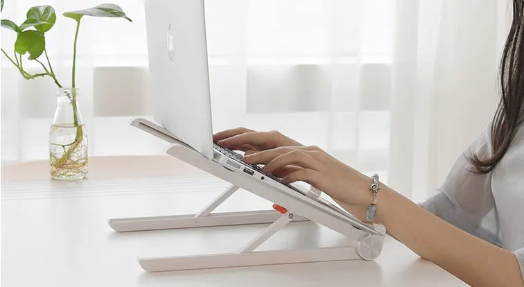 White foldable laptop stand on a desk, showing its elevated, angled position for ergonomic use.