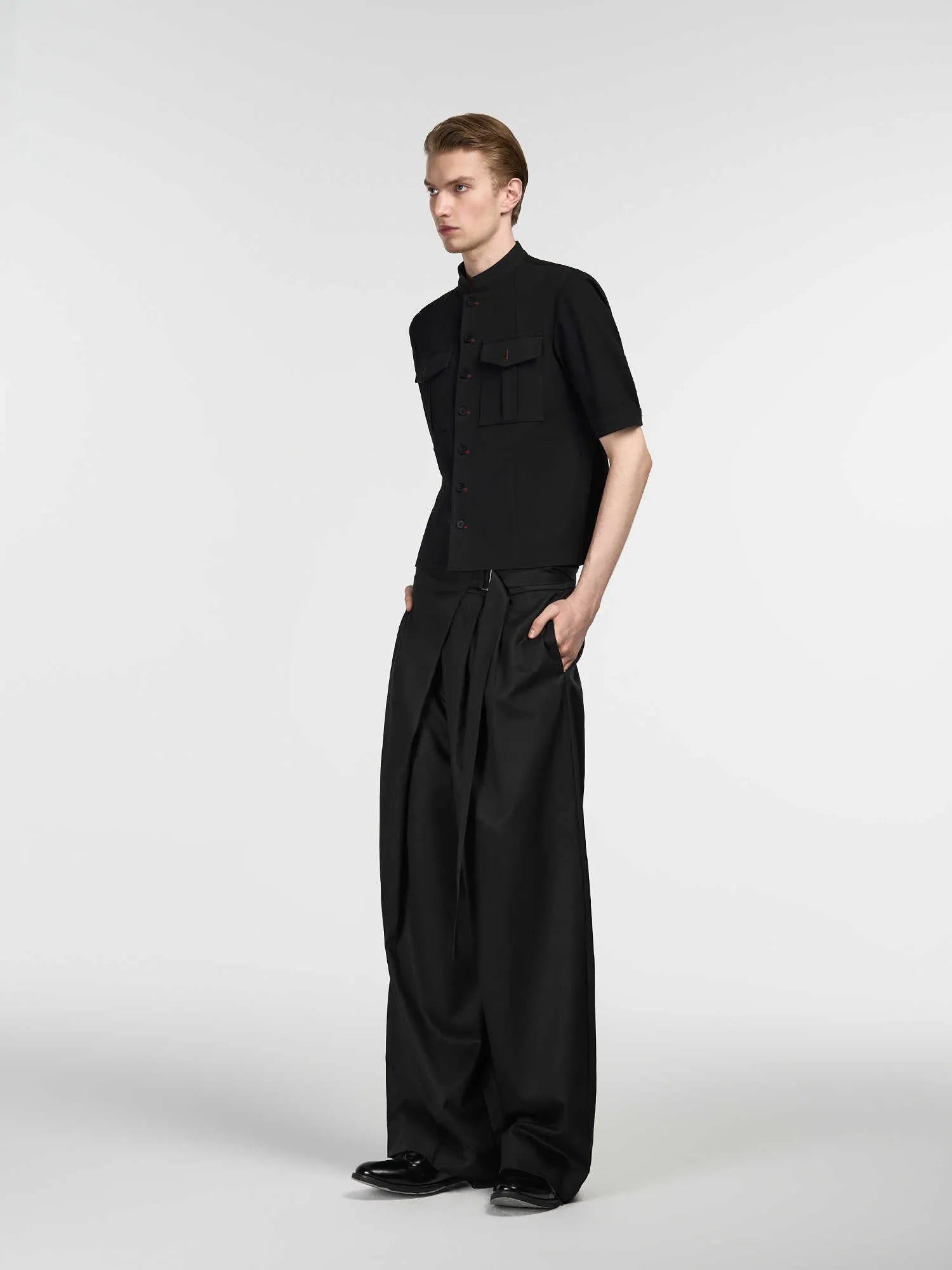 Black single pleated straight-leg trousers with an adjustable waistband on a hanger.