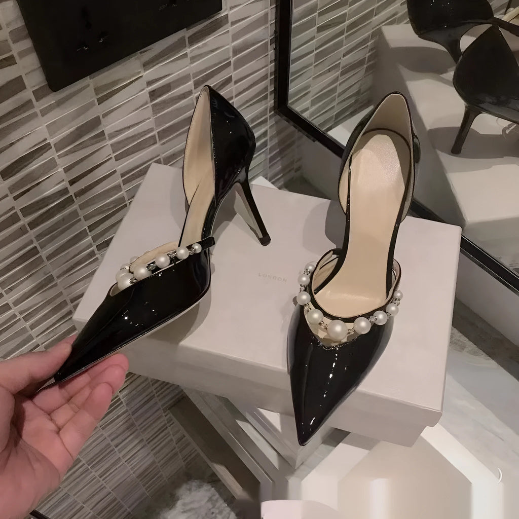 Women's black patent leather stiletto high heels with pointed toe and pearl decoration on display.