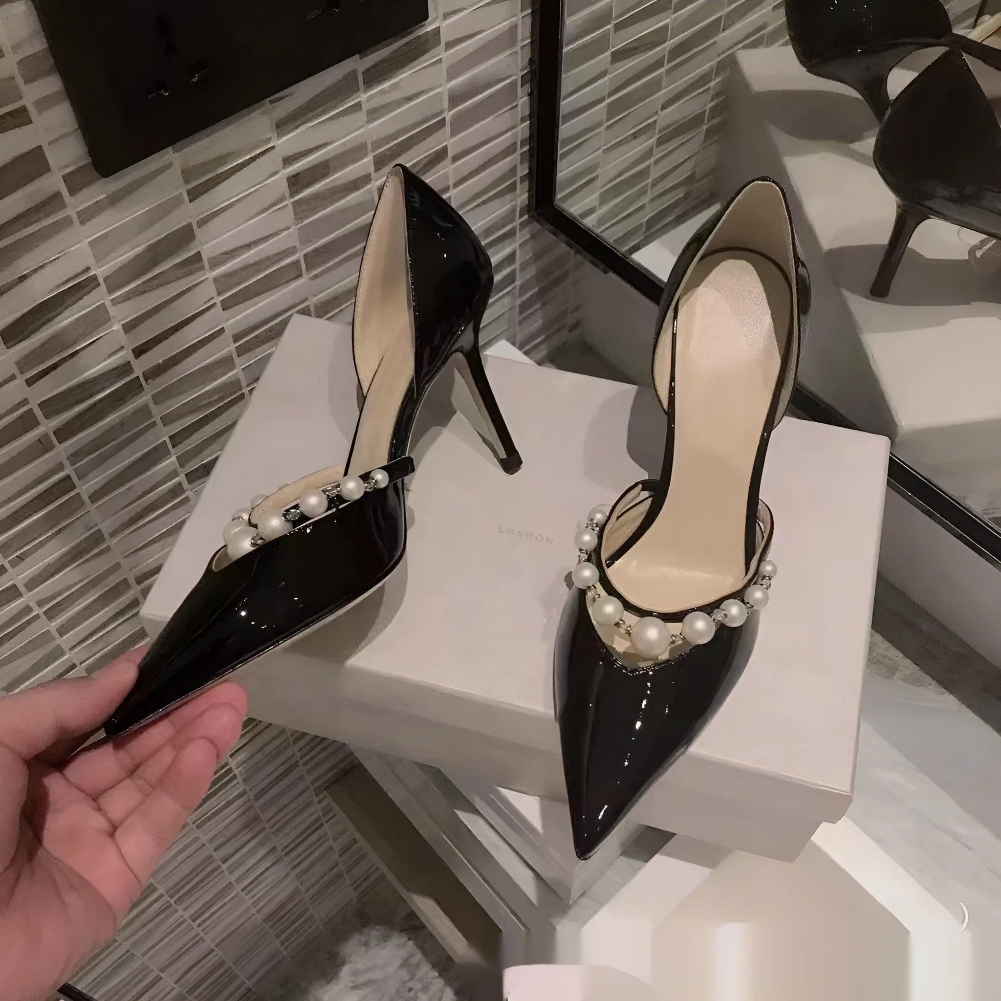 Women's black patent leather stiletto high heels with pointed toe and pearl decoration on display.