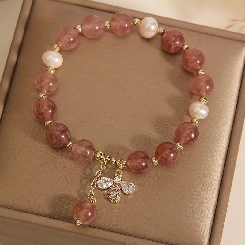 Adjustable pink strawberry quartz bracelet with three freshwater pearls and sparkling zircon charms on a wrist.