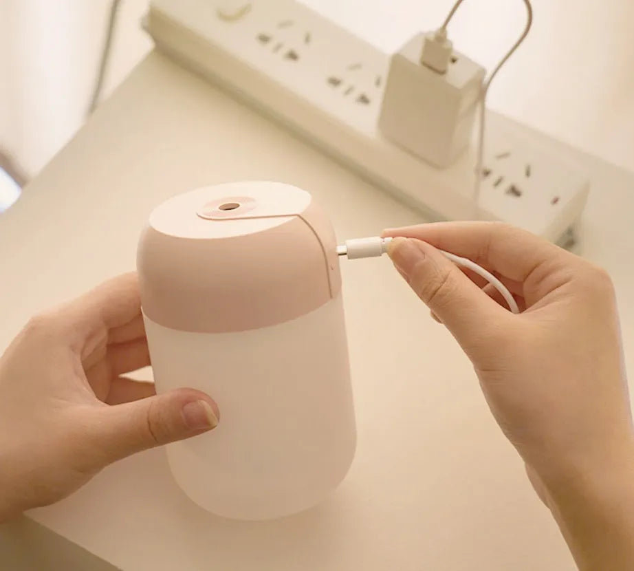 White cylindrical USB mini humidifier with charging cable on wooden desk