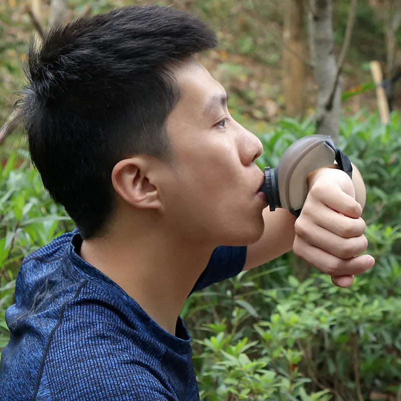Black silicone wrist water bottle with orange Velcro strap secured around a wrist, showing bite valve.