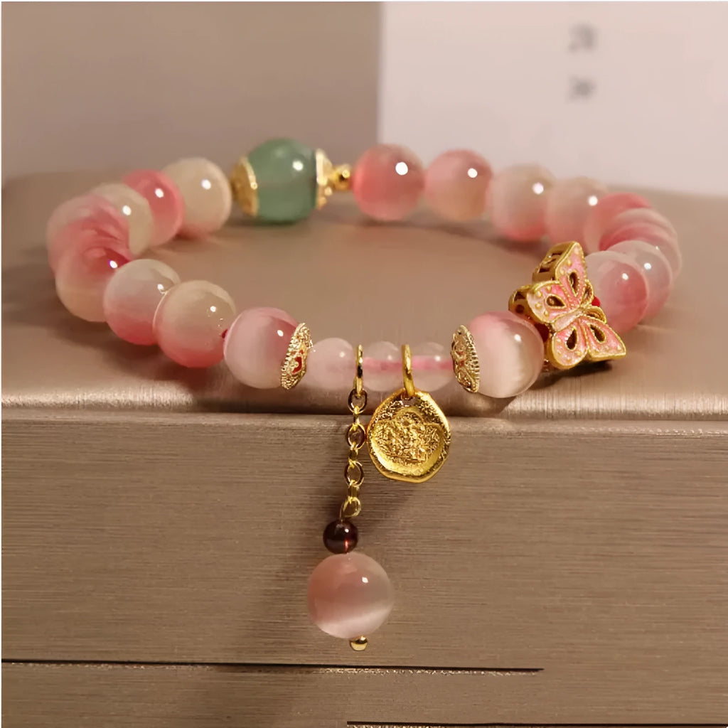Close-up of a women's bracelet with a pink opal butterfly charm on an electroplated chain.