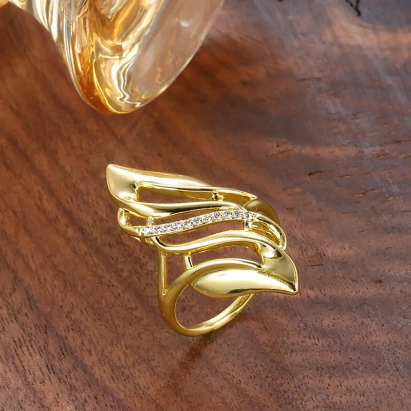 Gold tone women's ring with an exaggerated curved design on a model's finger.