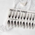 Close-up of long black and pink Christmas gothic nail tips with frosted finish on a flat surface, next to a storage strip.