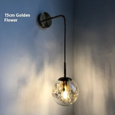 Modern glass wall mounted bedside lamp in golden flower finish on a white wall.