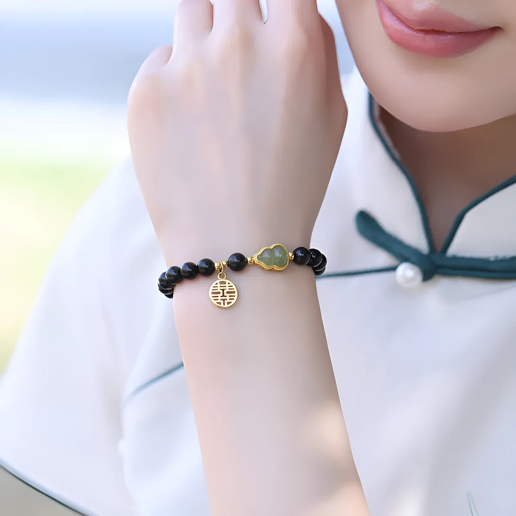 Black obsidian bead bracelet with a carved Hetian jade gourd charm, shown in geometric retro style.