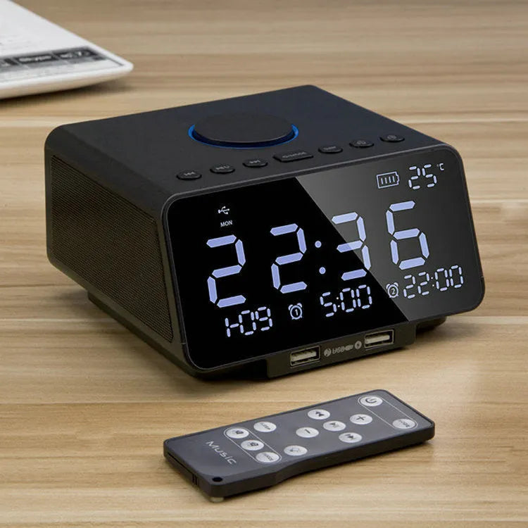 Black and white wireless alarm clock speaker with Bluetooth, radio, and USB playback functions on a bedside table.