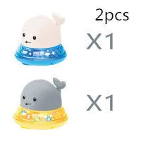 White and blue whale-shaped bath toy spraying water with LED lights on, floating in a baby bath