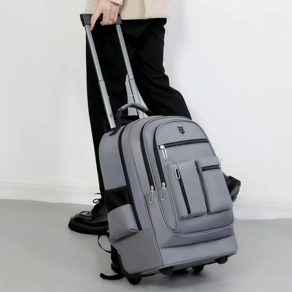 Large capacity multi layer travel backpack with wheels, black colour, standing on a flat surface with telescopic handle extended