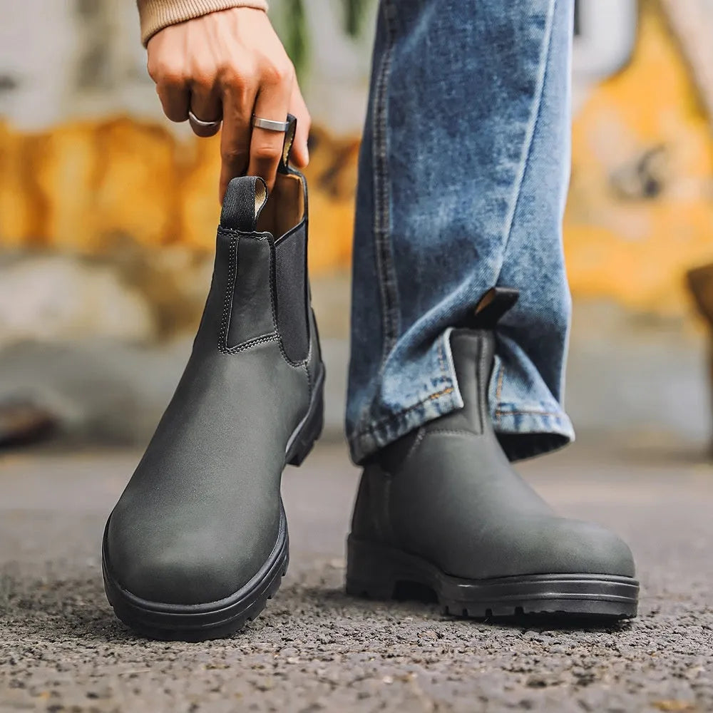 Vintage frosted brown leather Chelsea boots with round toe and car suture detailing on a wooden floor.