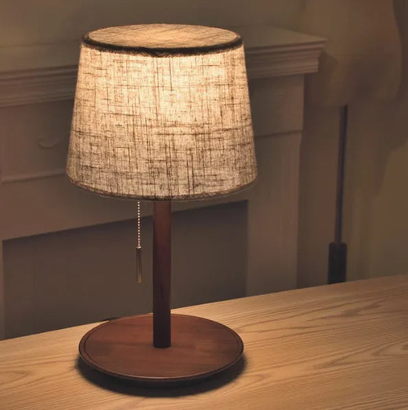 Walnut coloured solid wood bedside lamp with a white cloth shade and a cable switch.