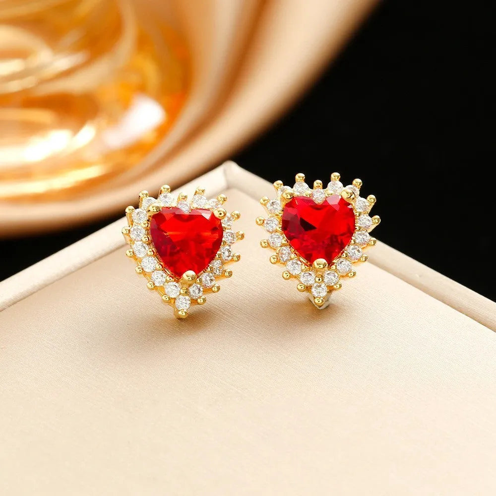 Gold red titanium steel necklace with heart and flower gemstone pendant, matching earrings, and ring on a grey background.