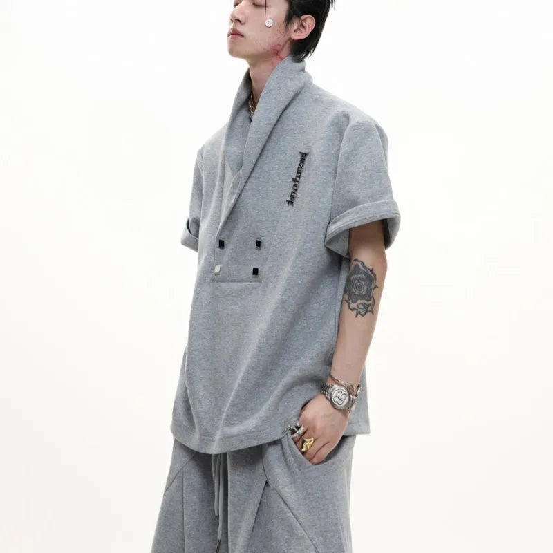 Men's dark grey cotton sports suit with V-neck top featuring padded shoulders and metal embellishments, paired with matching shorts.